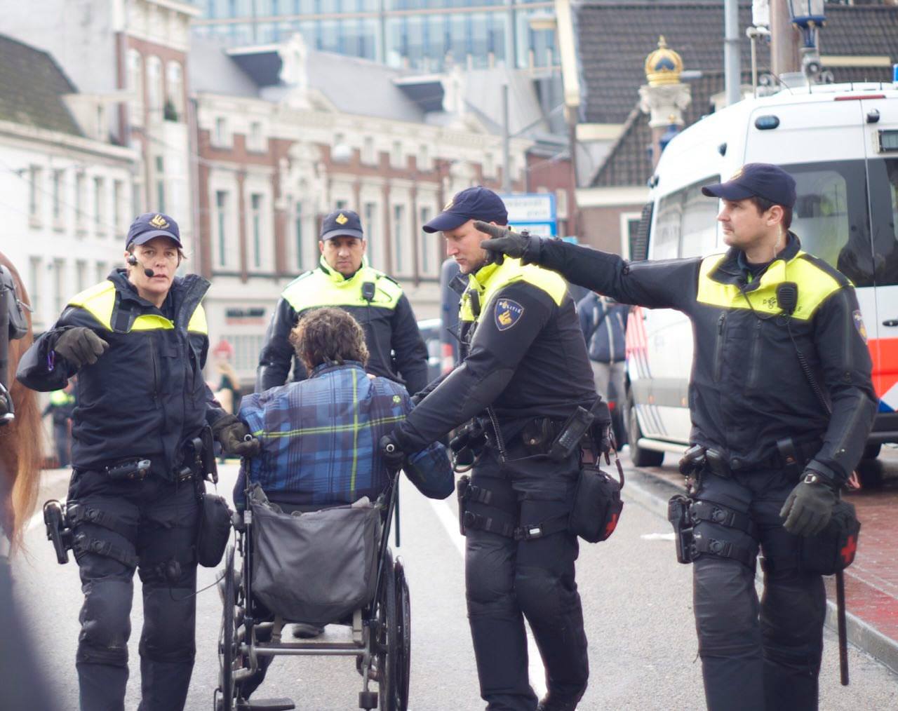 person in wheelchair escorted by 3 cops